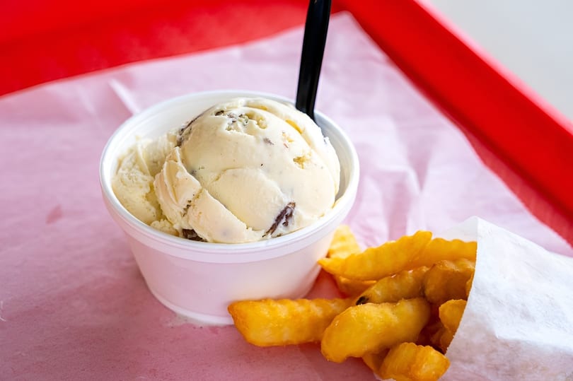 A cup of vanilla ice cream with chocolate chunks and a side of crinkle-cut fries.